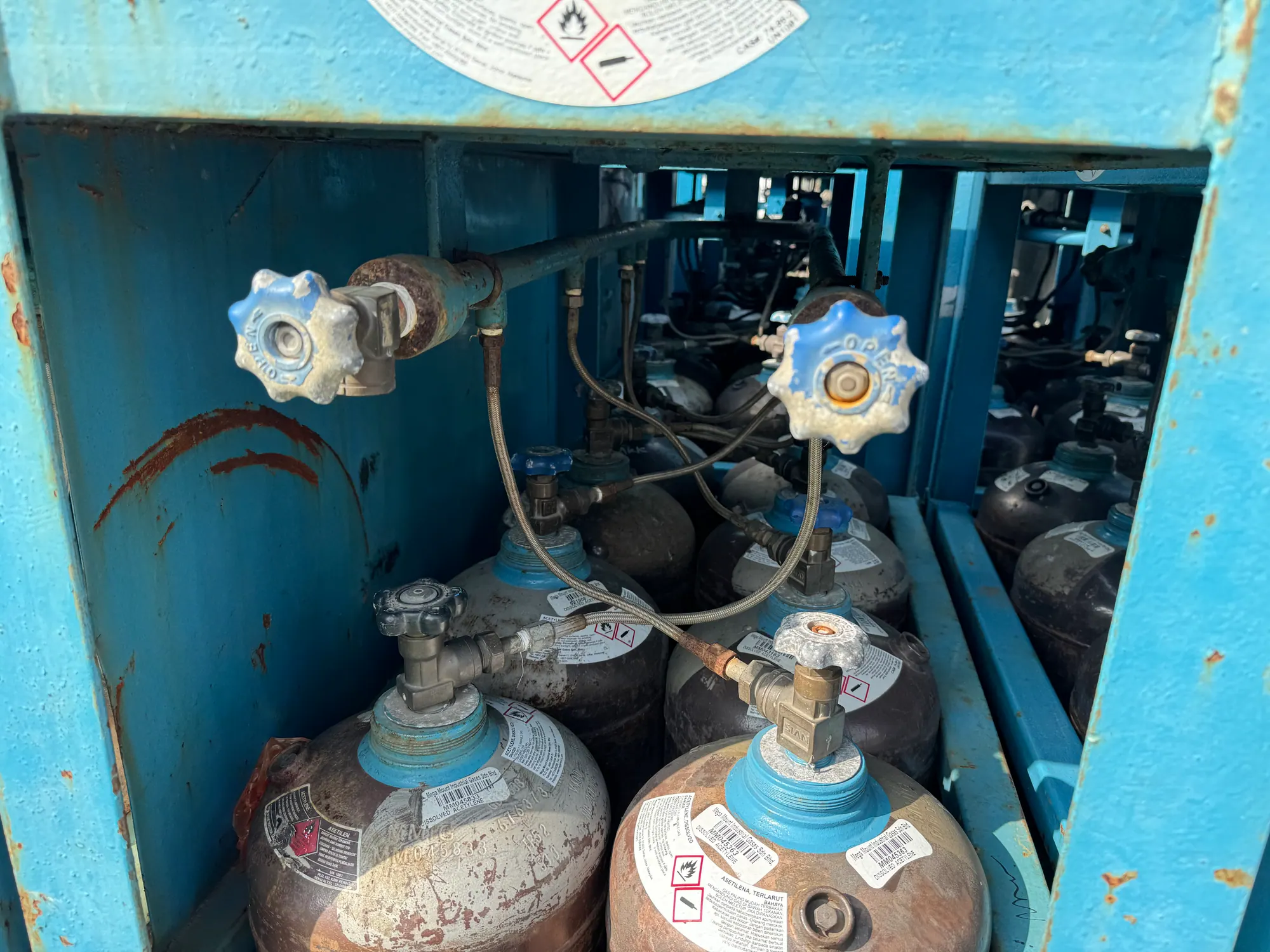 Acetylene cylinders manifolded together inside a blue steel cascade frame with flexible pigtails