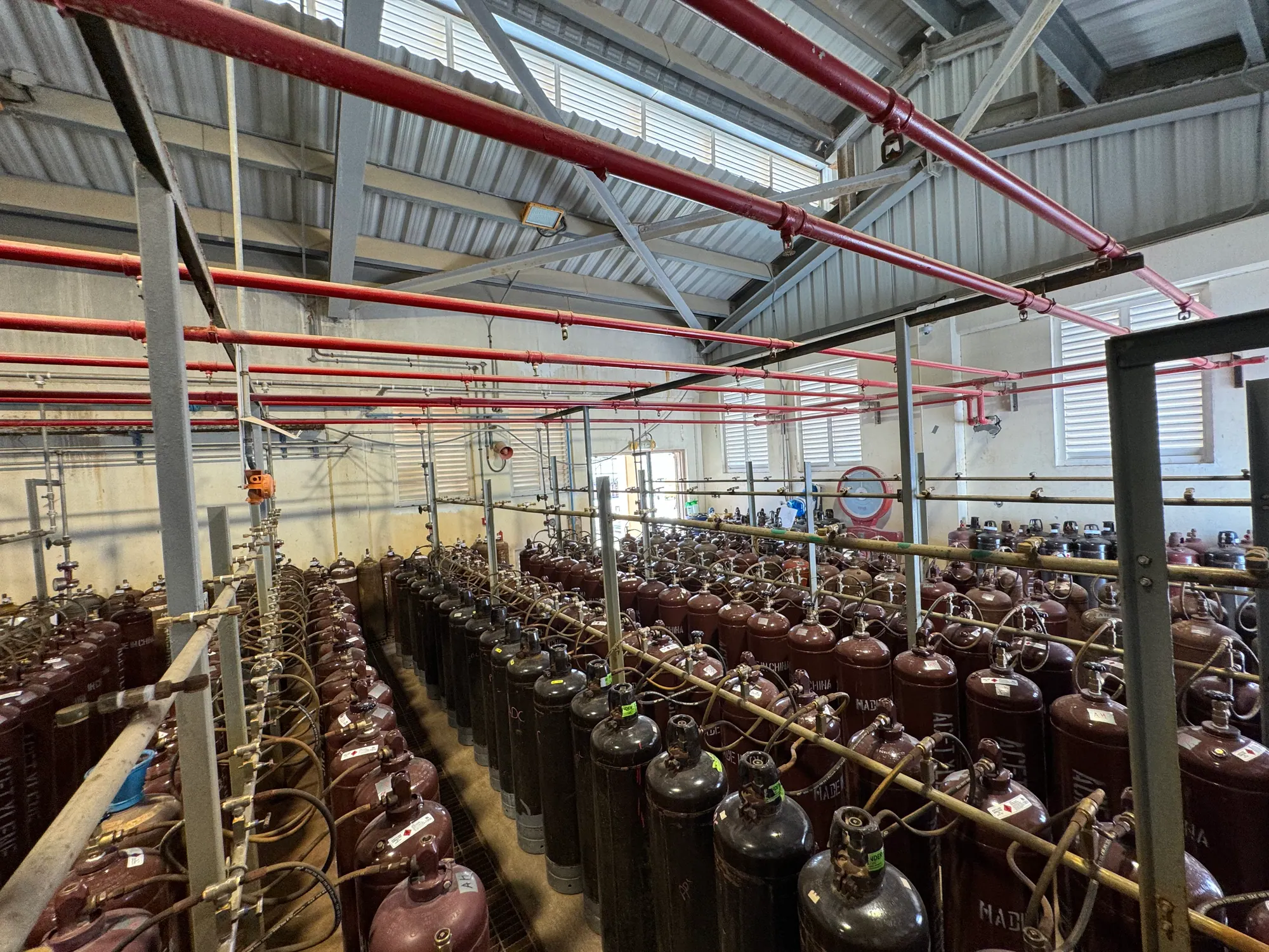 Rows of dissolved acetylene cylinders coupled to filling manifold hoses beneath overhead fire mains