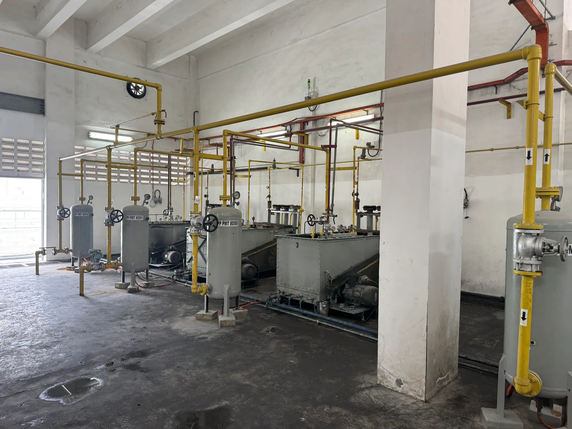 Gas plant room with a line of pressure vessels, yellow service pipework and process skids